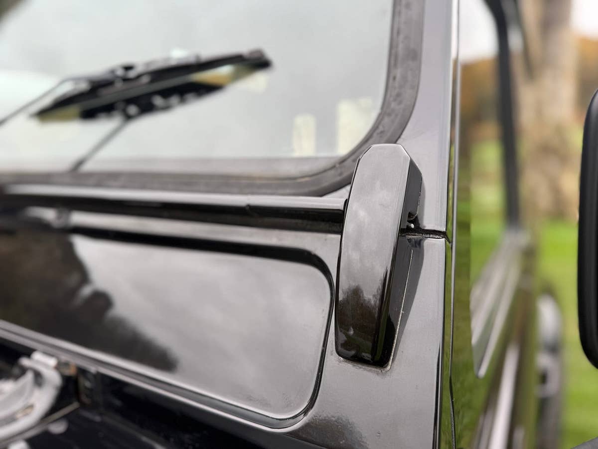Deep gloss black paintwork across the bonnet and screen surround of a finished Defender