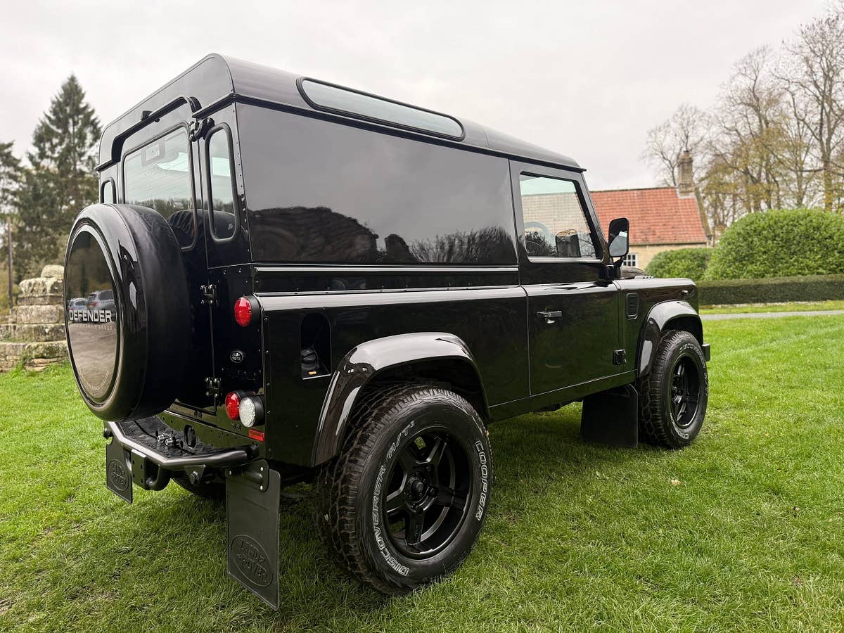 A black Defender 90 on grass beside a stone abbey