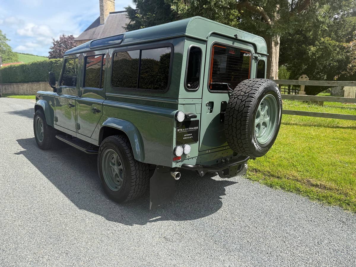 A heritage-green StraightRange Defender 110 on a village lane