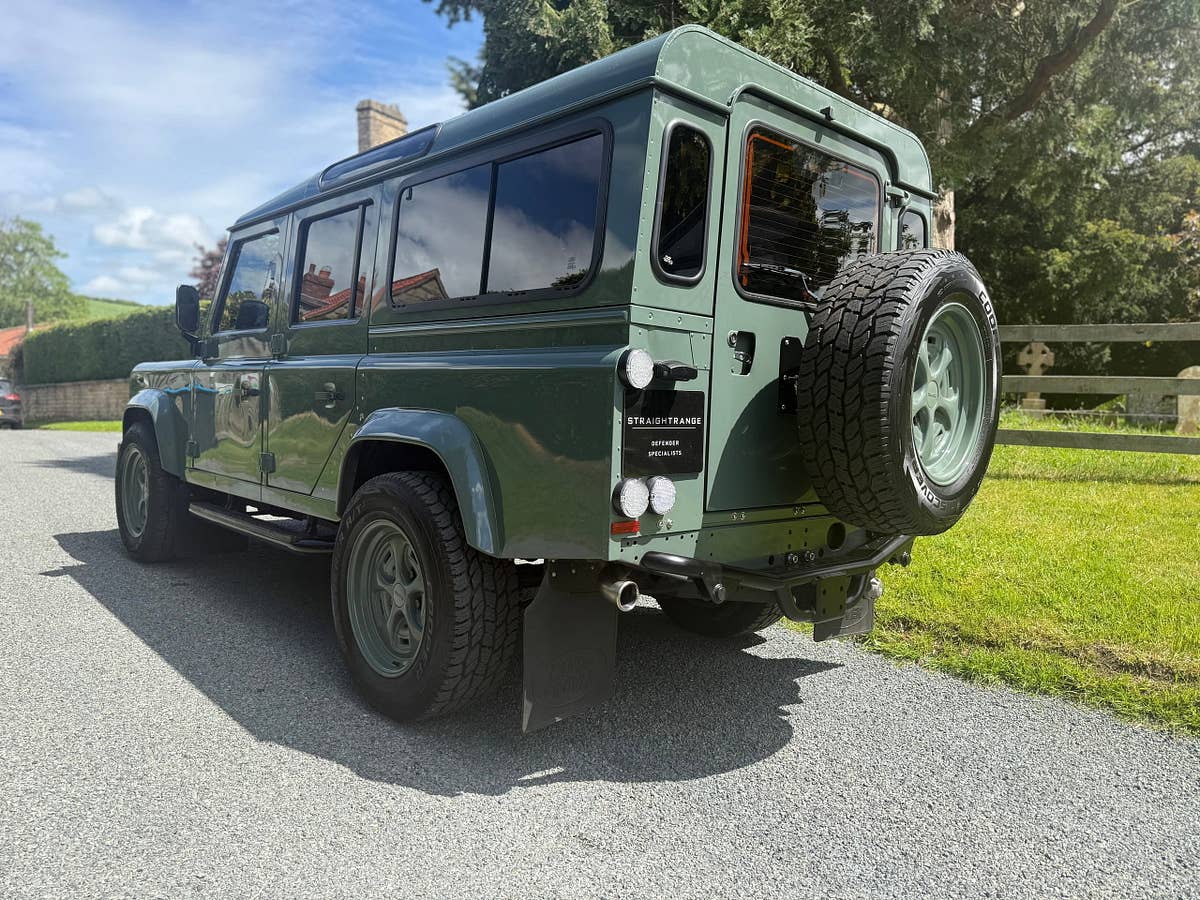 A heritage-green StraightRange Defender 110 on a village lane