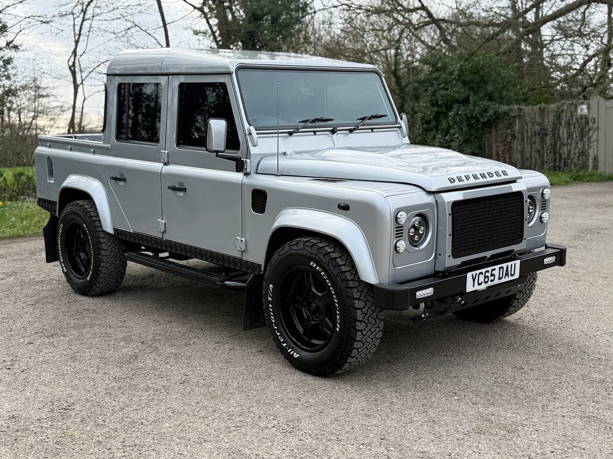 A silver Defender 110 double-cab pickup on a tree-lined lane